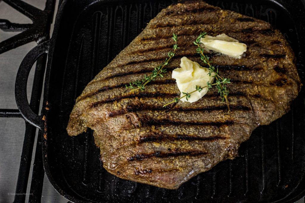 grilled flank steak in a cast iron grill pan topped with butter and thyme