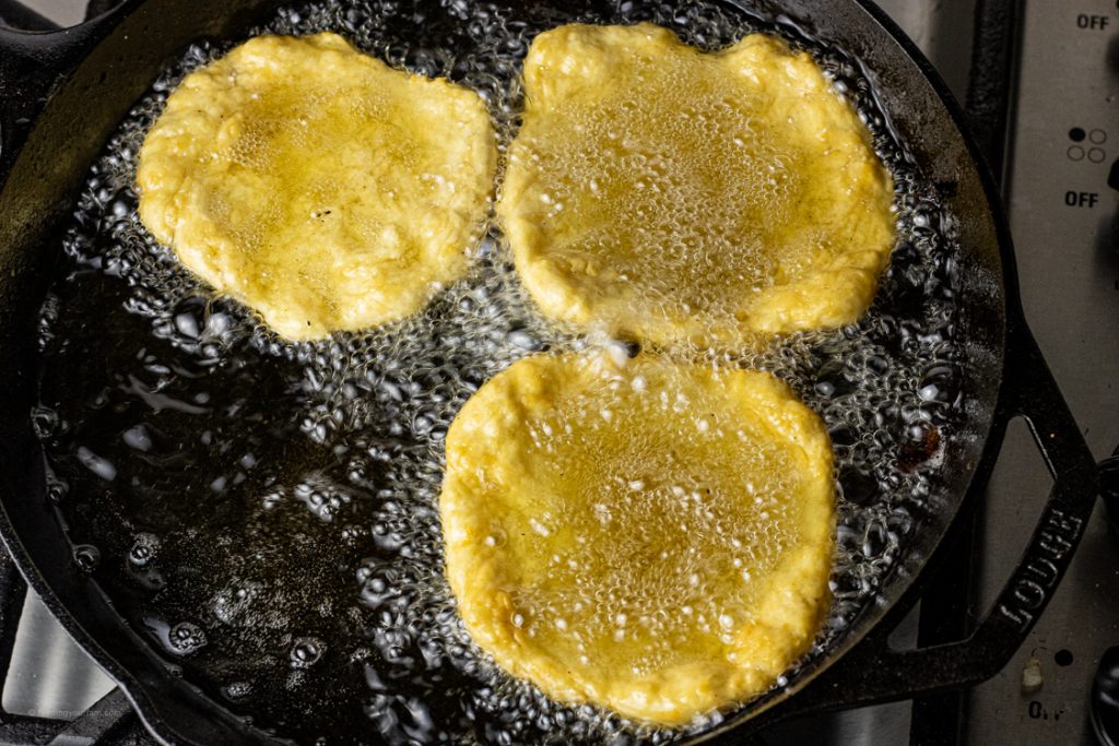 round pieces of dough frying in oil in a cast iron pan