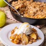 fresh apple crisp with an oatmeal cookie topping on a white plate topped with a scoop of vanilla ice cream