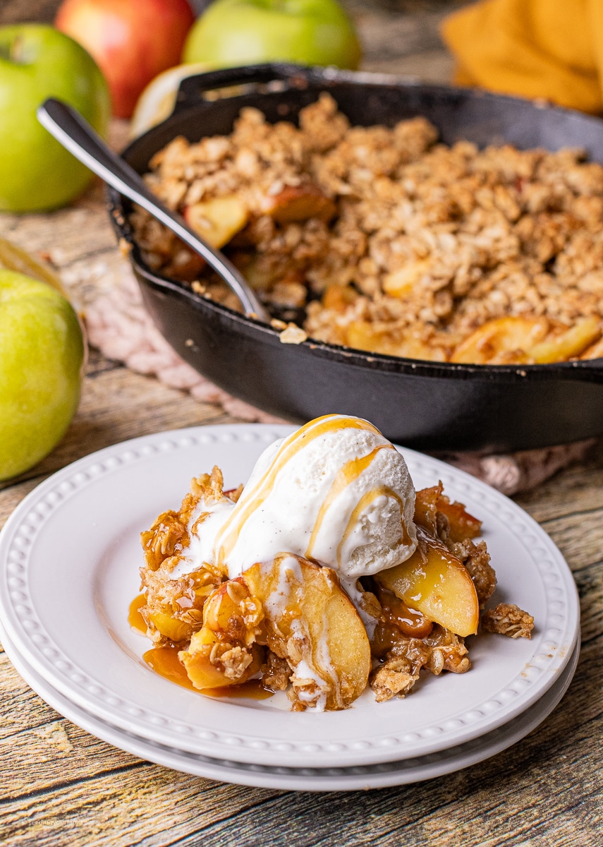 fresh apple crisp with an oatmeal cookie topping on a white plate topped with a scoop of vanilla ice cream