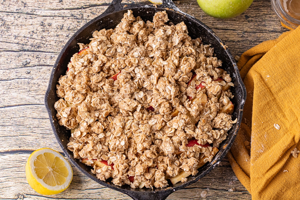 uncooked apple crisp with an oatmeal cookie topping in a cast iron skillet.
