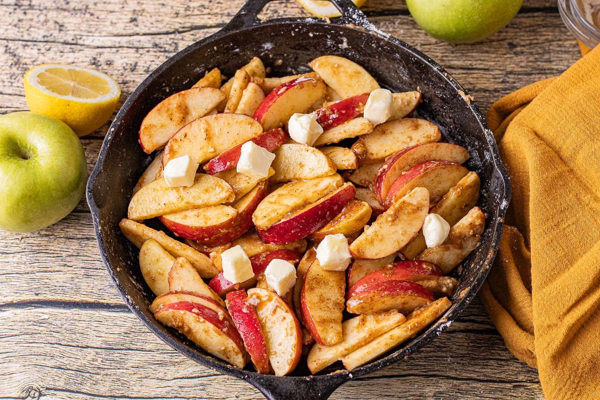 apples coated in flour, sugar and spices in a cast iron skillet to make apple crisp