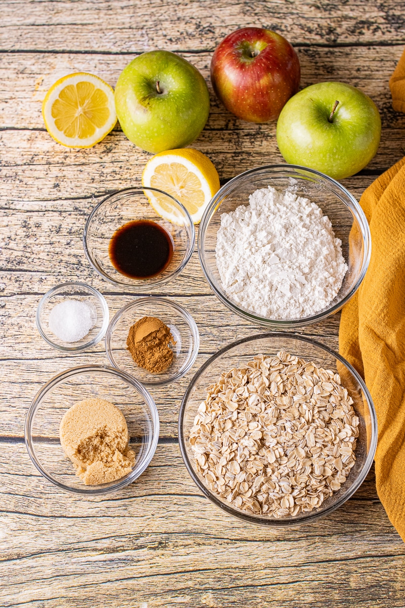 bowls of ingredients for apple crisp like oats, flour, vanilla, brown sugar, cinnamon and salt.