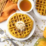 pumpkin waffles on a white plate topped with whipped cream
