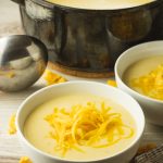 big pot of cheesy cauliflower soup surrounded by two smaller white bowls filled with soup and topped with shredded cheese