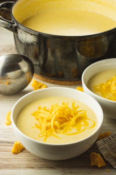 big pot of cheesy cauliflower soup surrounded by two smaller white bowls filled with soup and topped with shredded cheese