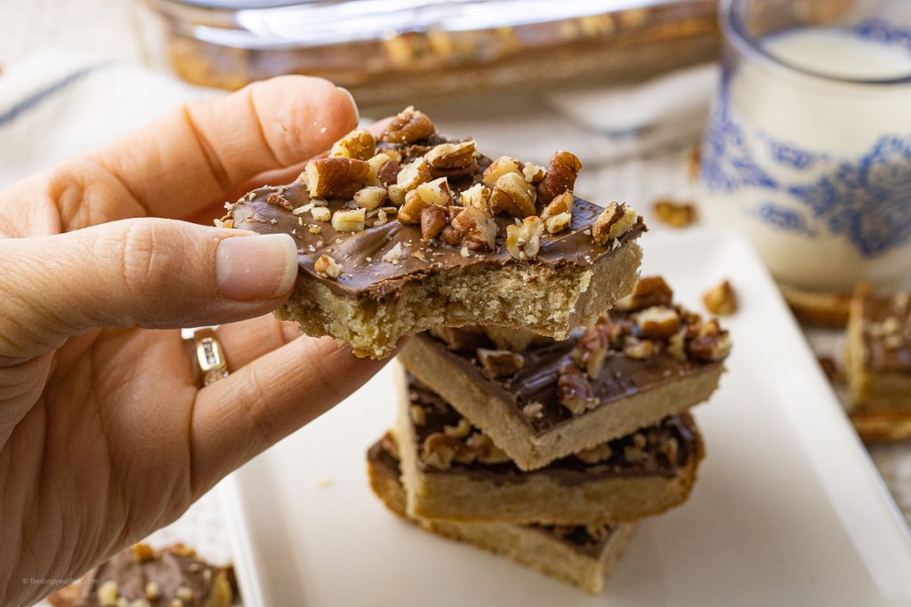 hand holding a shortbread cookie topped with chocolate and nuts with a bite out of it