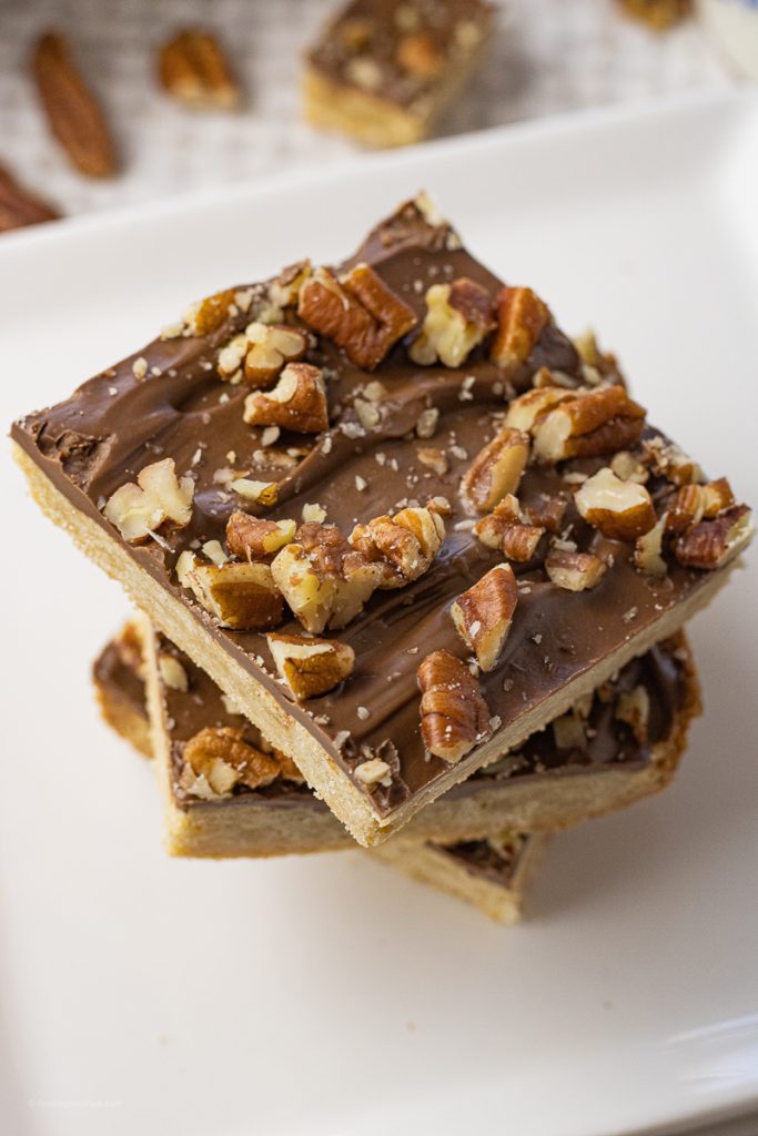 stack of shortbread crust topped with chocolate and chopped pecans