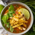 bowl of tortilla soup topped with lime, cilantro and tortilla strips