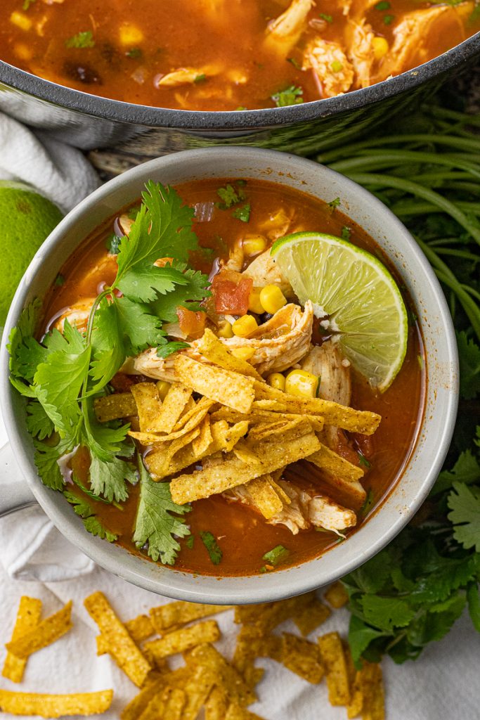 grey bowl with tortilla soup topped with tortilla strips, lime and cilantro