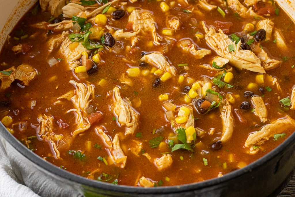 big pot of shredded chicken in tomato broth with black beans, corn and cilantro to make tortilla soup