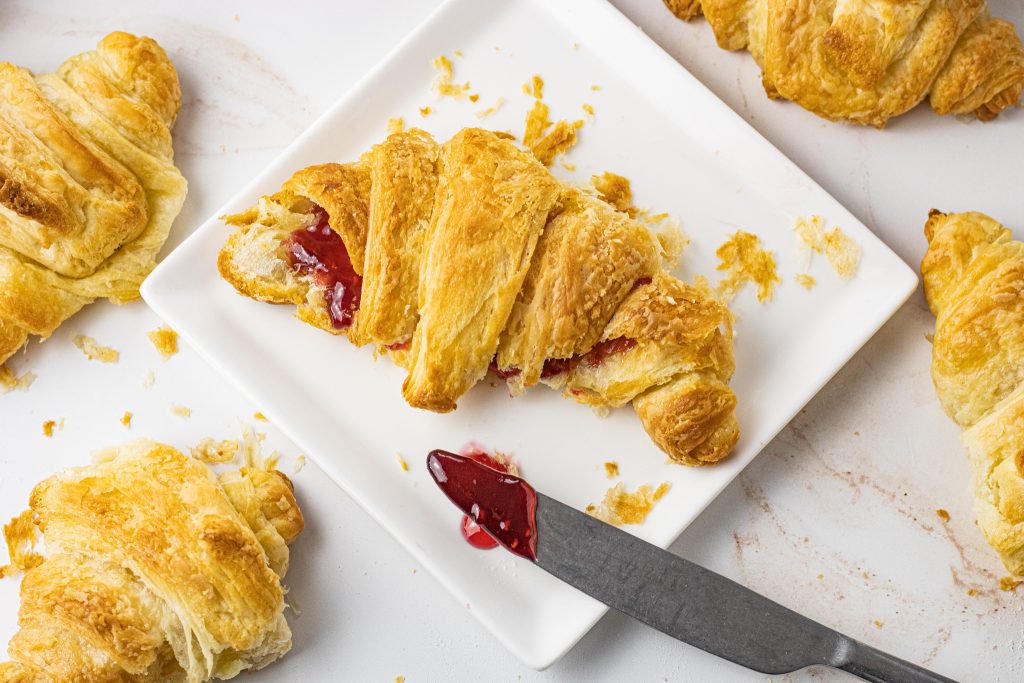 flaky croissants with jam on a white plate