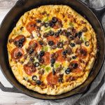 pizza topped with pepperoni, sausage, olives and green peppers in a cast iron pan
