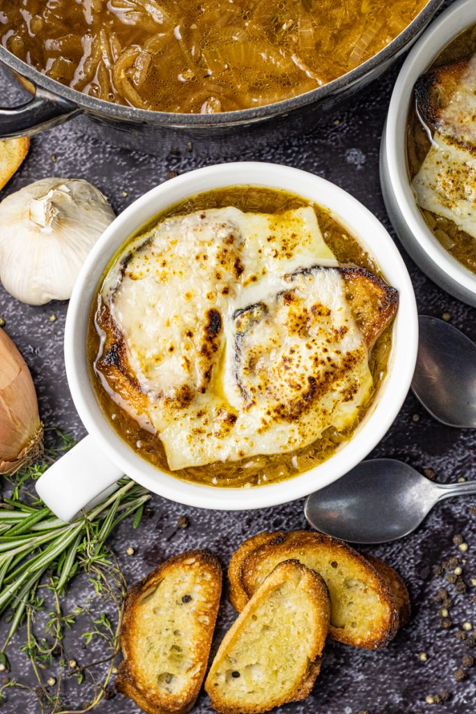 white bowl of onion soup topped with bread and a slice of Swiss cheese
