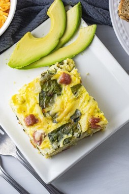 square slice of egg casserole with spinach, ham and hash browns on a white square plate