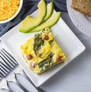 square slice of egg casserole with spinach, ham and hash browns on a white square plate
