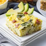 piece of breakfast casserole with hash browns, egg, cheese and spinach on a white plate