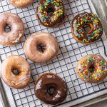 glazed and chocolate topped donuts with colorful sprinkles on a cooling rack on top of a baking sheet