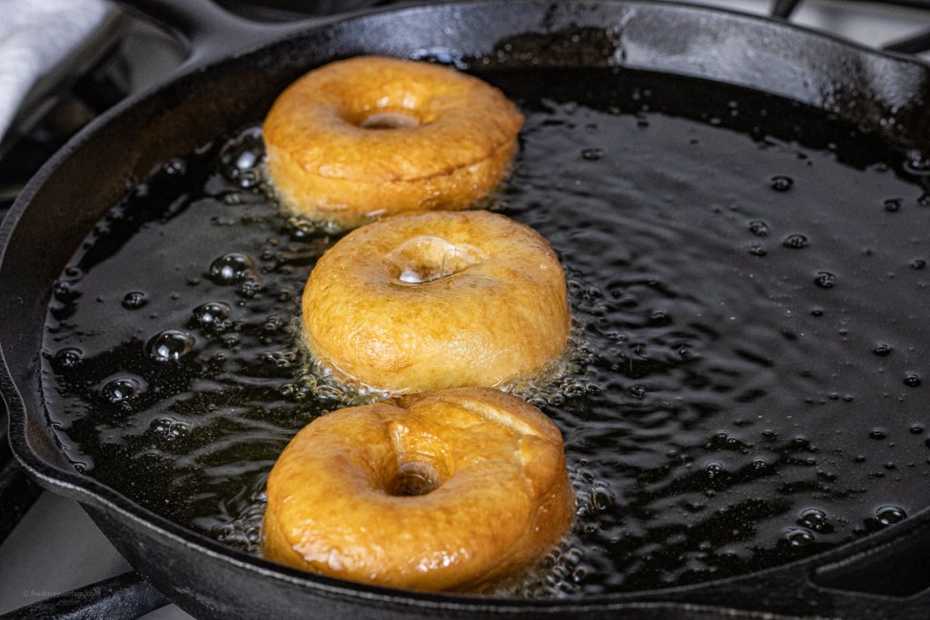 golden brown donuts frying in oil in a black cast iron pan