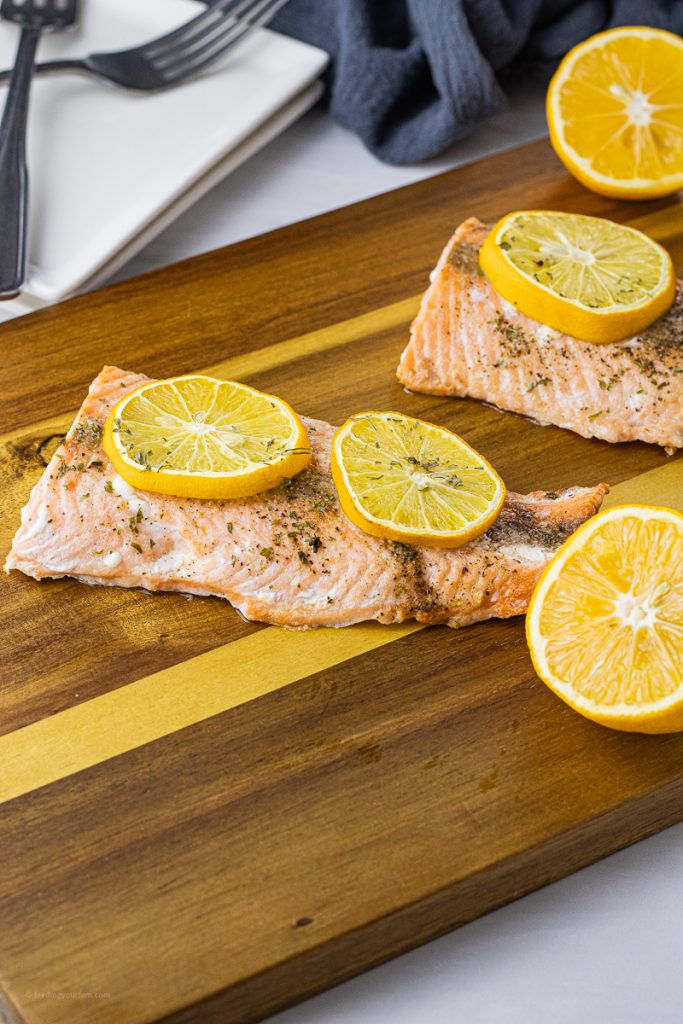 cooked salmon filets topped with lemon slices on a wooden cutting board