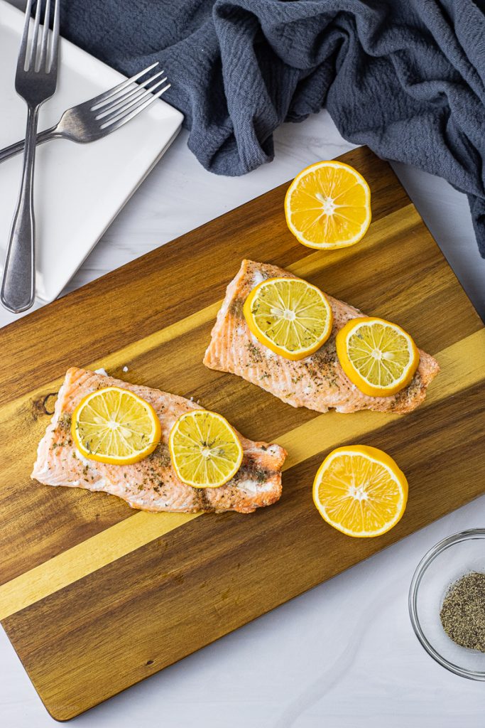 salmon topped with lemon slices on a wooden cutting board