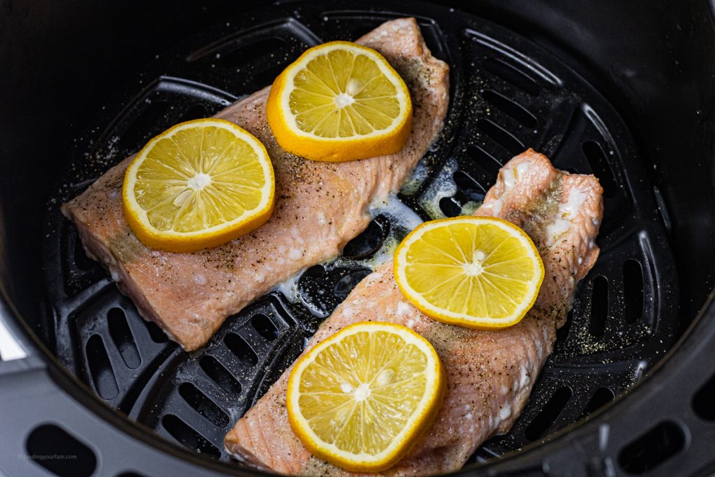 salmon filets in the basket of an air fryer topped with lemon slices