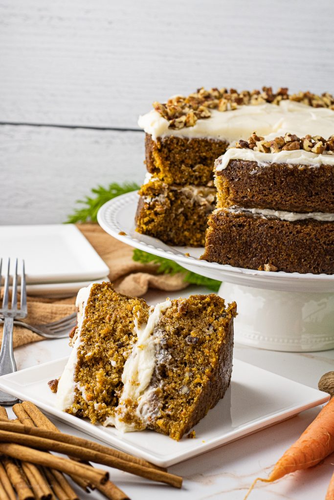 slice of carrot cake on a white plate with the whole carrot cake in the background
