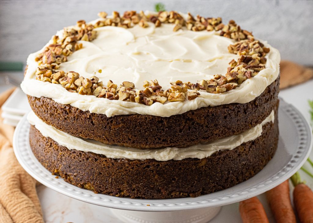 two layer carrot cake topped with cream cheese frosting and chopped pecans