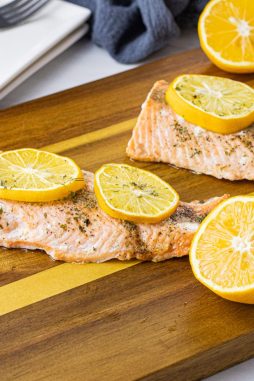 cooked salmon pieces topped with lemon slices on a wooden cutting board