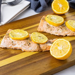 cooked salmon pieces topped with lemon slices on a wooden cutting board