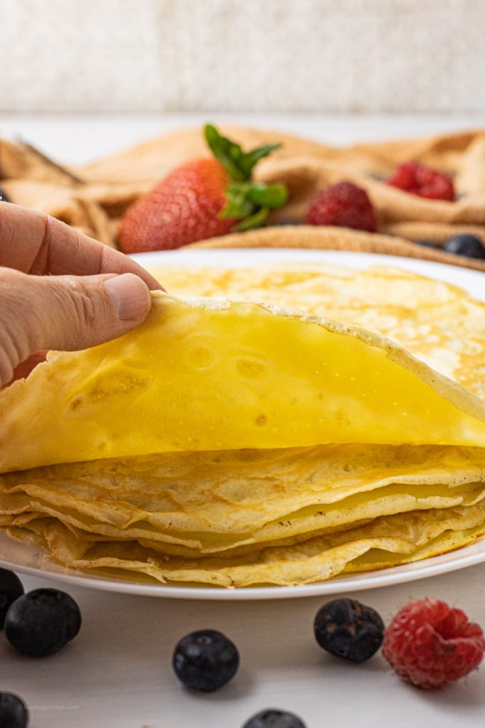 stack of crepes on a white plate with a hand lifting the top crepe