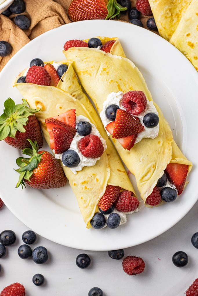 two crepes filled with berries and whipped cream on a white plate