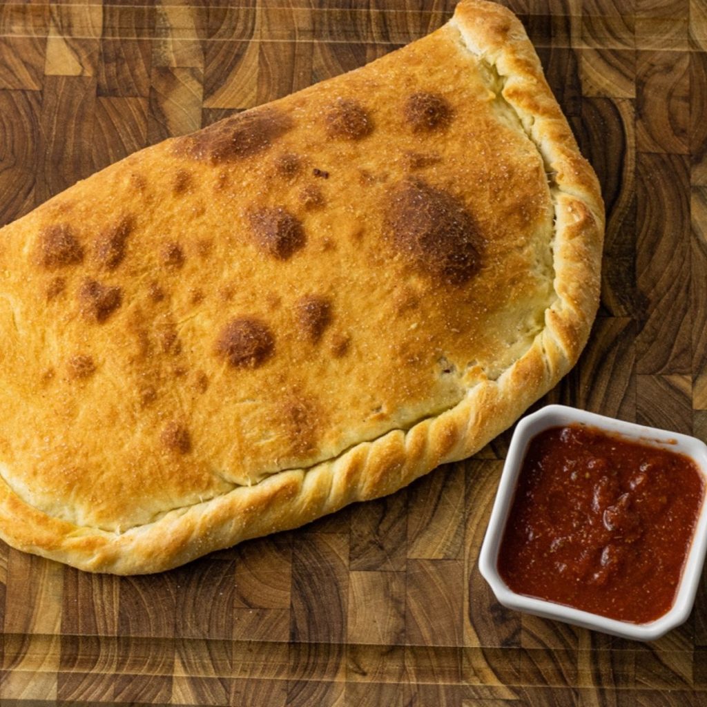 calzone on a wooden cutting board with pizza sauce