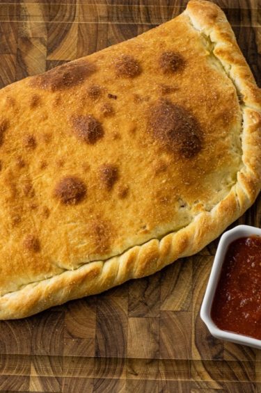 calzone on a wooden cutting board with pizza sauce