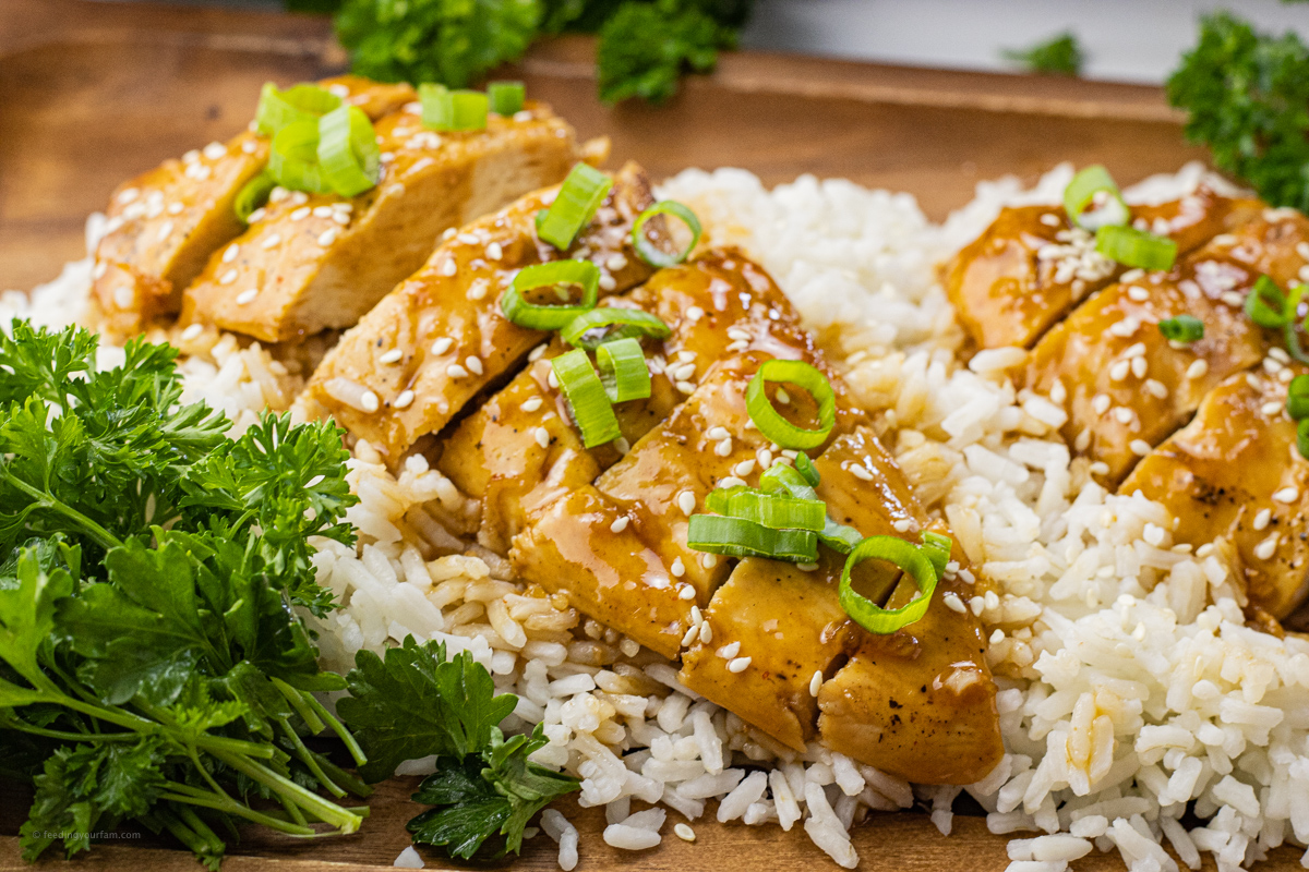 sliced chicken covered in sauce and topped with sliced green onions, sesame seeds and on rice