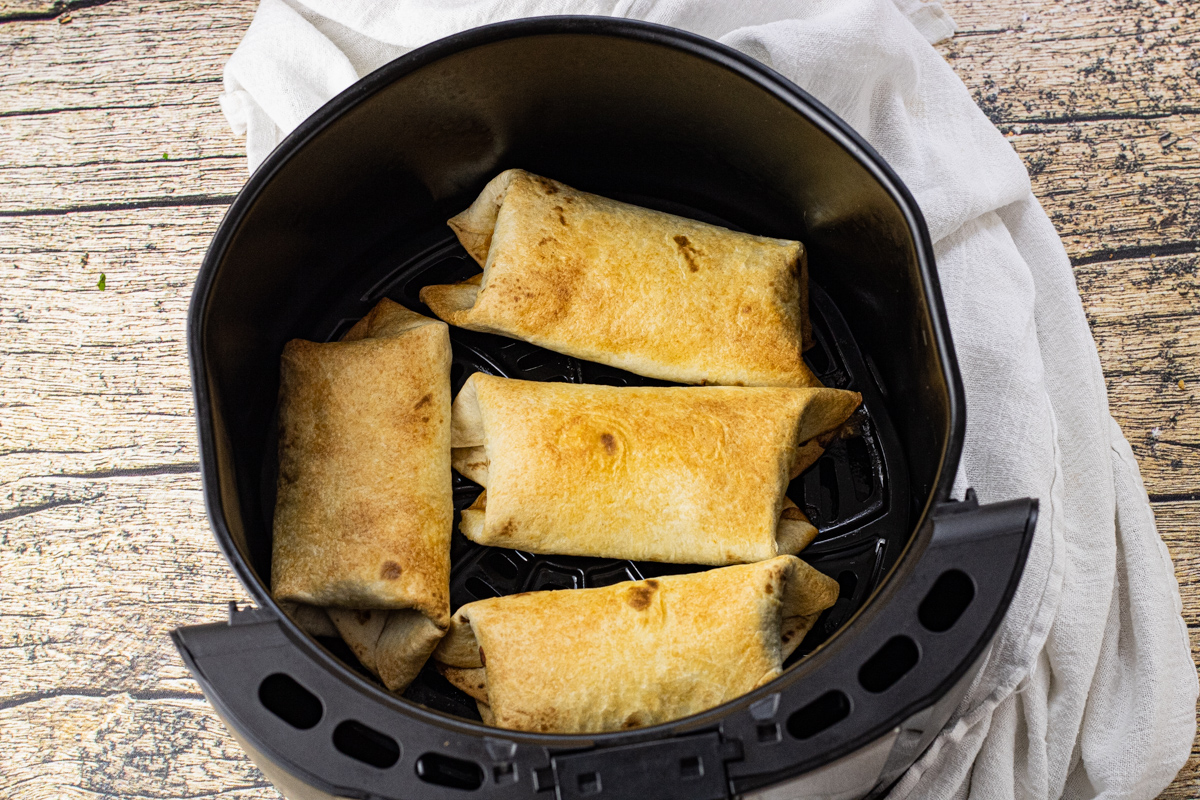 golden brown rolled up chimichangas in an air fryer basket