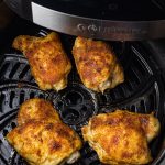 seasoned chicken thighs in the basket of an air fryer