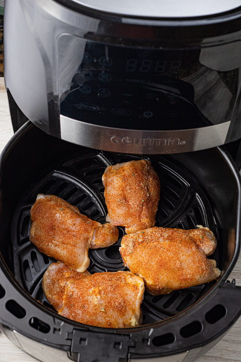 seasoned, uncooked chicken thighs in the basket of a black air fryer