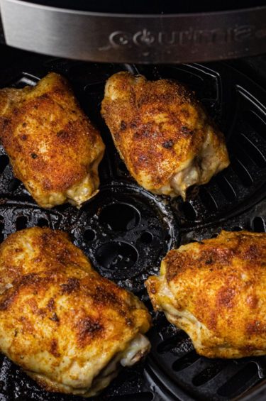 cooked chicken thighs in the basket of an air fryer