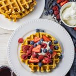 waffle on a white plate topped with fresh berries and whipped cream
