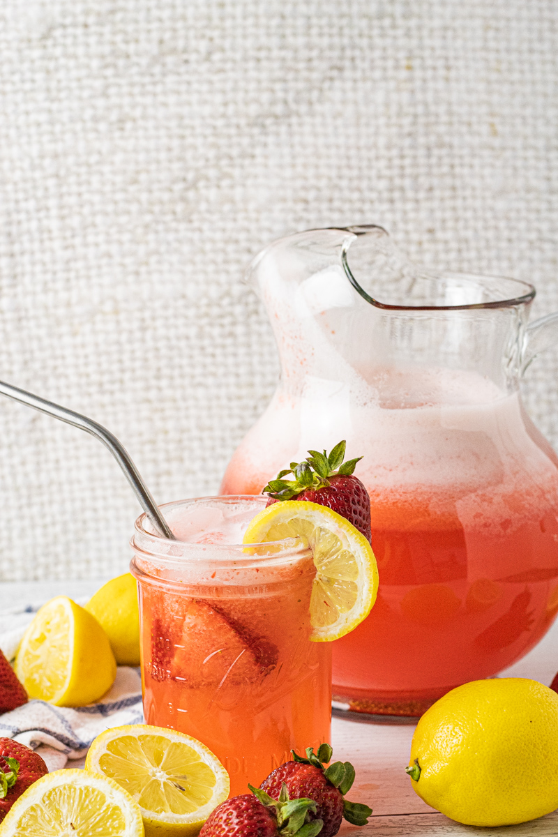 pitcher of strawberry lemonade with a small jar filled with strawberry lemonade and a metal straw