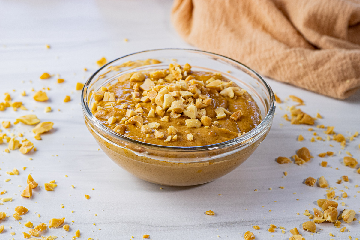 small glass bowl filled with peanut butter sauce topped with crushed peanuts