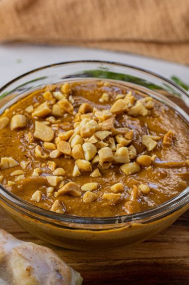bowl of peanut sauce in a glass bowl topped with chopped peanuts