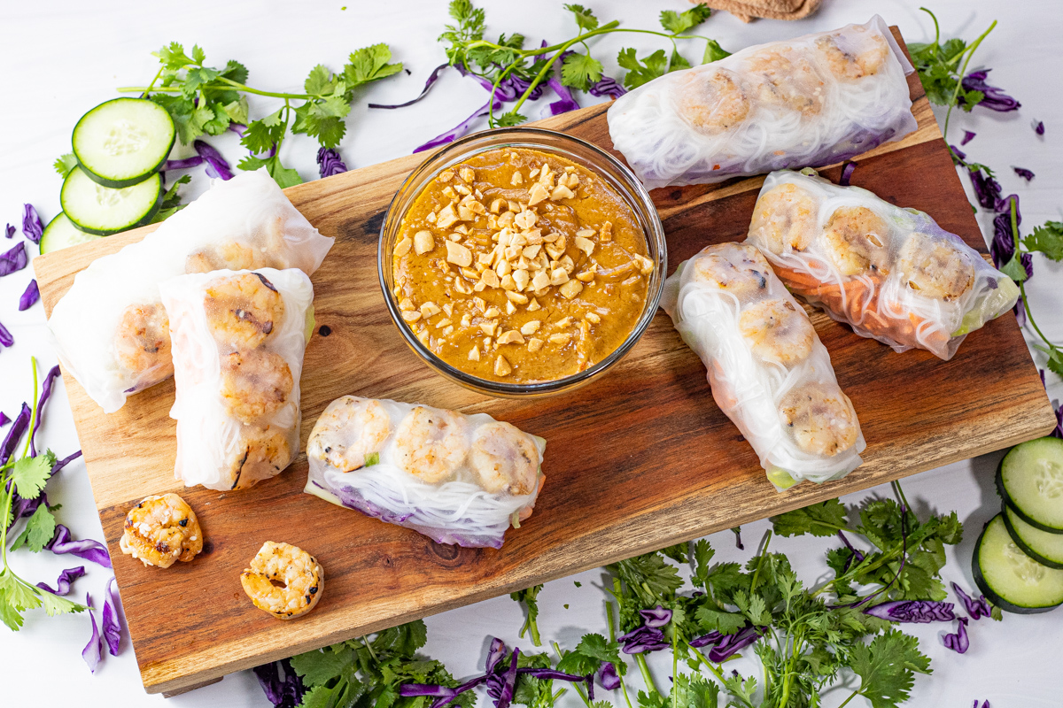 shrimp spring rolls on a wooden platter with peanut dipping sauce