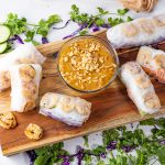 spring rolls on a wooden platter with a peanut butter dipping sauce in the center