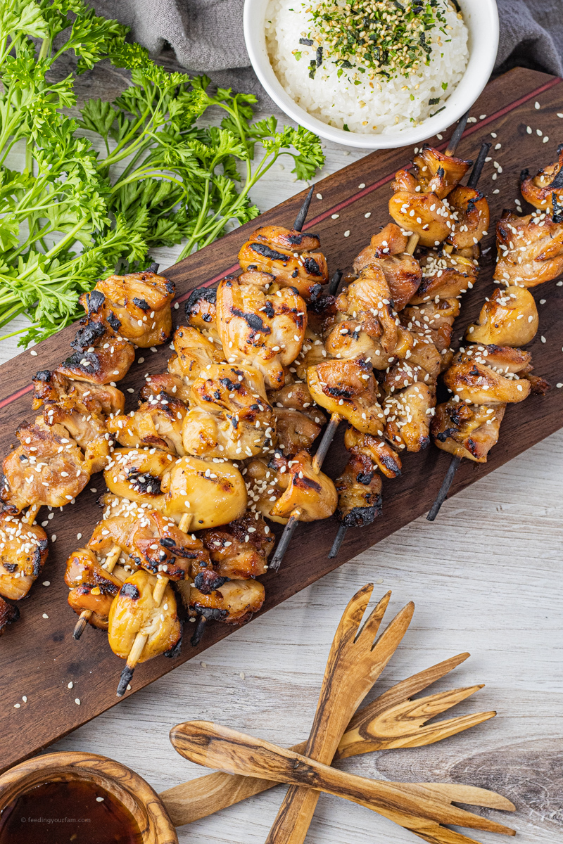 chicken kabobs that have been grilled and topped with sesame seeds on a dark wooden board