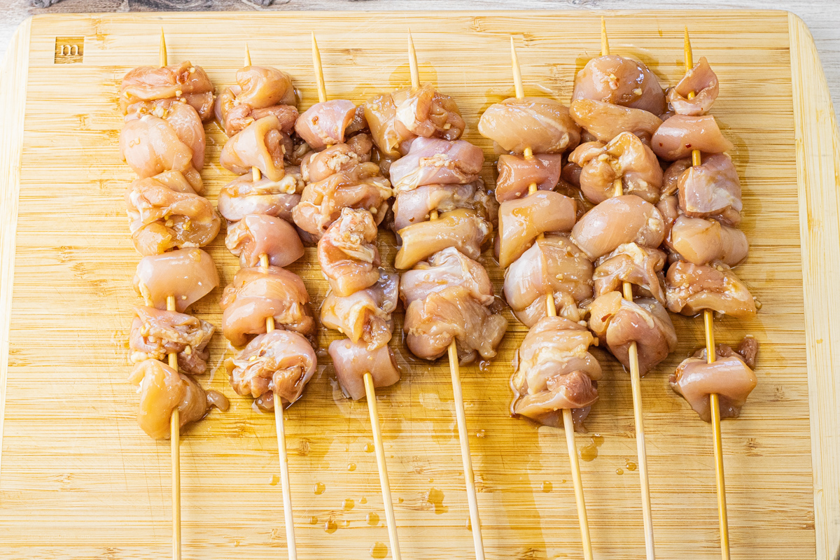 raw chicken threaded on wooden skewers on a wooden cutting board