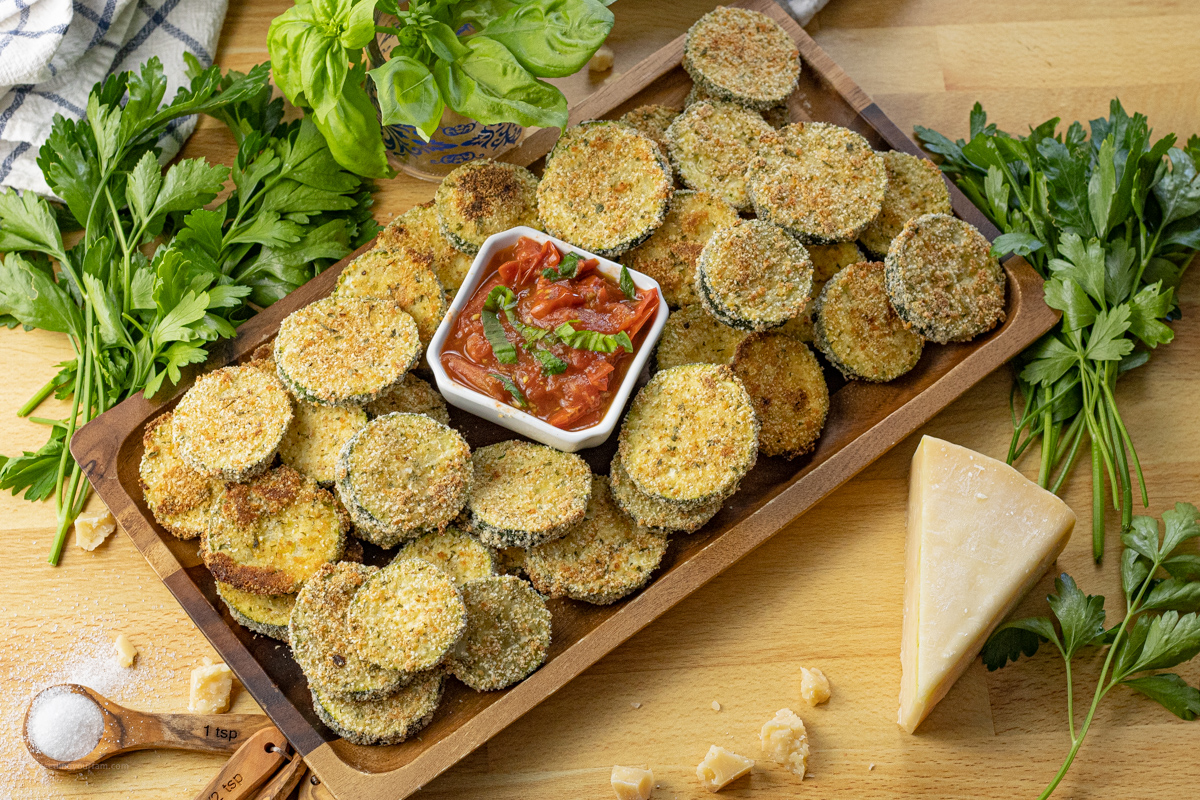 baked zucchini rounds on a wooden platter with a tomato basil dipping sauce