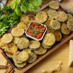 zucchini rounds baked with bread crumbs on a wooden platter with a tomato basil dipping sauce