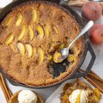 peach cobbler in a cast iron pan with some scooped out